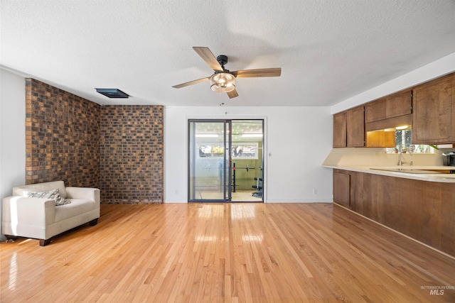 unfurnished living room featuring brick wall, a textured ceiling, a ceiling fan, and light wood-style floors