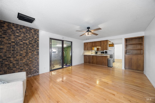 unfurnished living room with light wood-type flooring, ceiling fan, and a textured ceiling