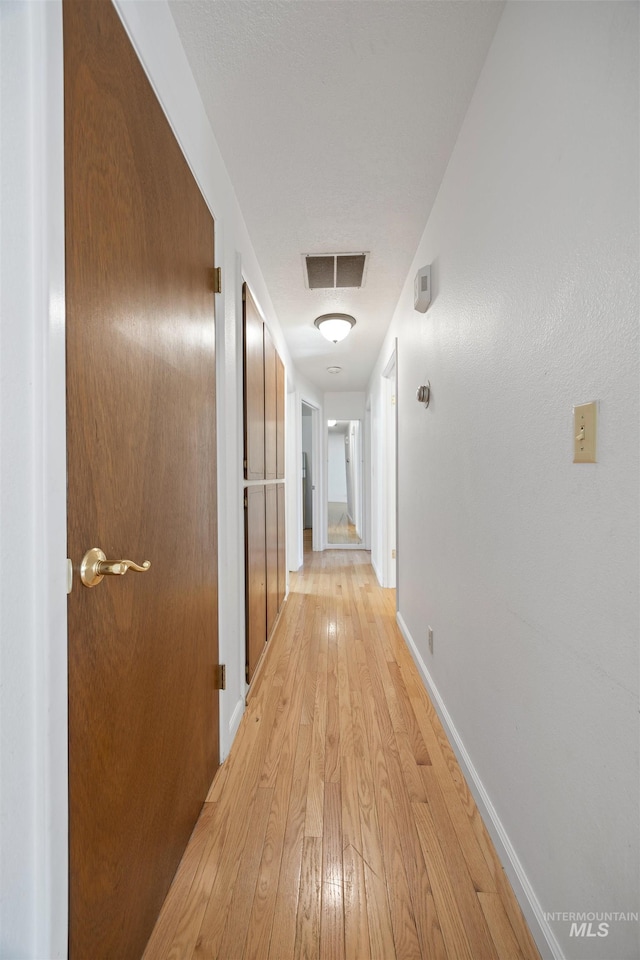 corridor featuring visible vents, light wood-style flooring, and baseboards