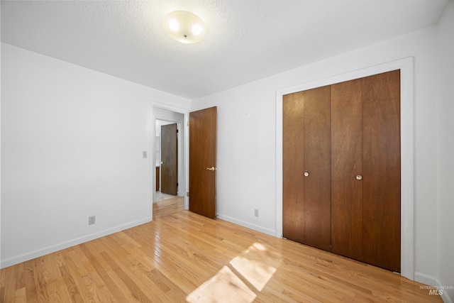 unfurnished bedroom featuring a textured ceiling, a closet, light wood-type flooring, and baseboards
