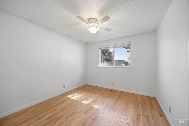 empty room with a textured ceiling, visible vents, a ceiling fan, baseboards, and light wood-style floors