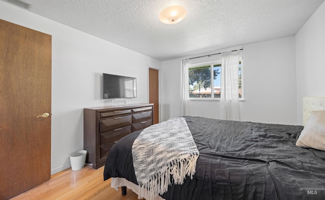 bedroom with baseboards, light wood-style flooring, visible vents, and a textured ceiling