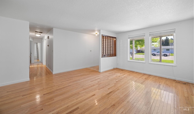 unfurnished room featuring baseboards, light wood-style flooring, visible vents, and a textured ceiling
