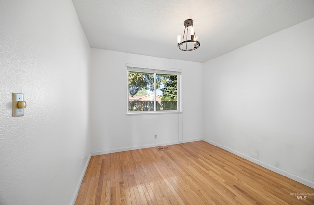 unfurnished room with an inviting chandelier, light wood-type flooring, visible vents, and baseboards