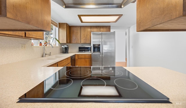 kitchen featuring a sink, brown cabinetry, black appliances, light countertops, and range hood