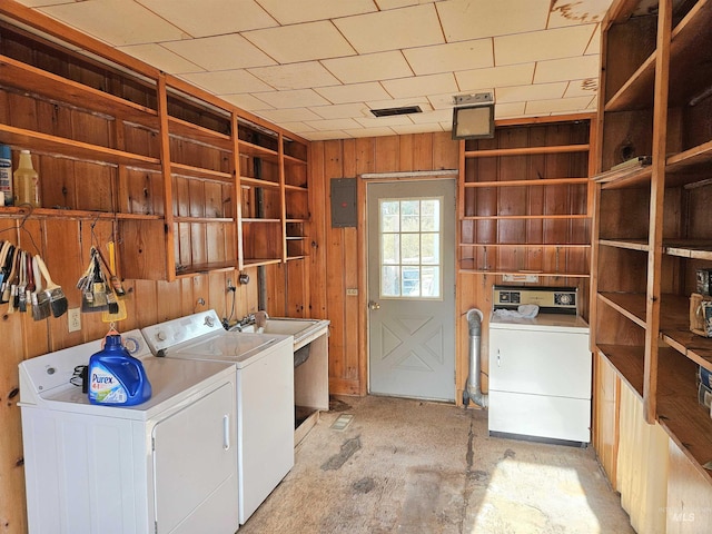 laundry area with electric panel, wood walls, and independent washer and dryer