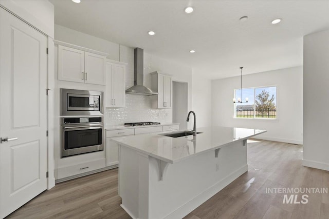 2158 N Kenora Ave, Star, ID 83669 - kitchen with appliances with stainless steel finishes, wall chimney exhaust hood, a kitchen island with sink, a chandelier, and white cabinets