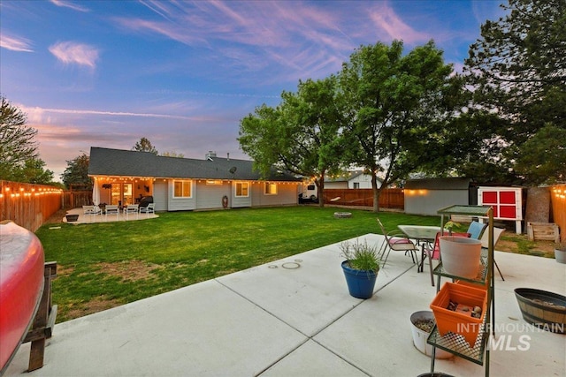 patio terrace at dusk with a storage unit, a fenced backyard, a lawn, and outdoor dining area