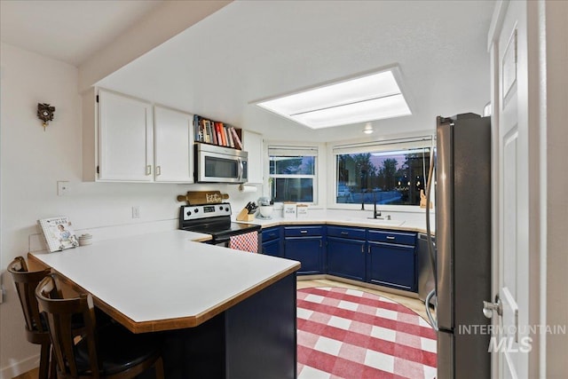 kitchen featuring a peninsula, a breakfast bar area, light countertops, appliances with stainless steel finishes, and blue cabinetry
