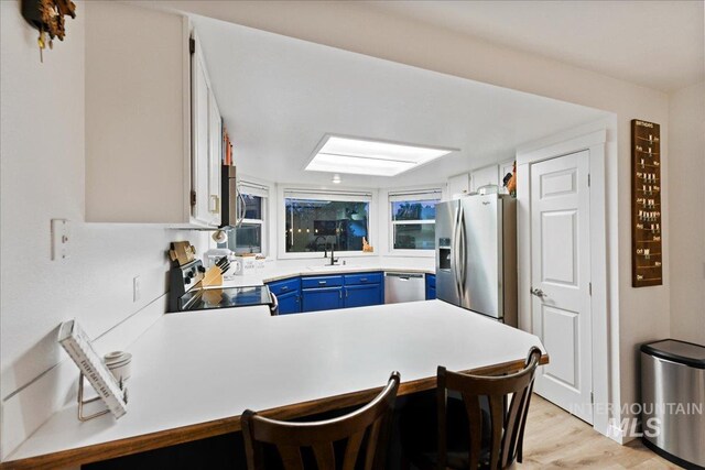 kitchen with a peninsula, a breakfast bar area, light countertops, blue cabinets, and stainless steel appliances