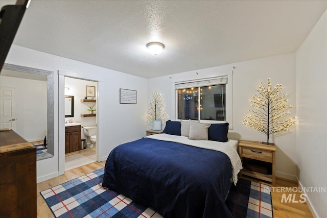bedroom featuring ensuite bathroom, baseboards, a textured ceiling, and wood finished floors