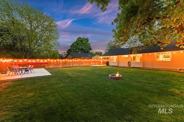 yard at dusk featuring fence, a patio, and a fire pit