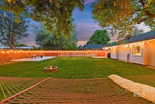 yard at dusk with a fenced backyard, a fire pit, and a patio area