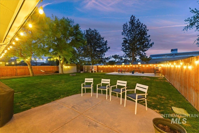 patio terrace at dusk featuring a yard, an outdoor structure, a fenced backyard, and a storage unit