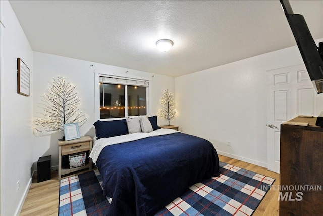 bedroom with light wood-type flooring, a textured ceiling, and baseboards