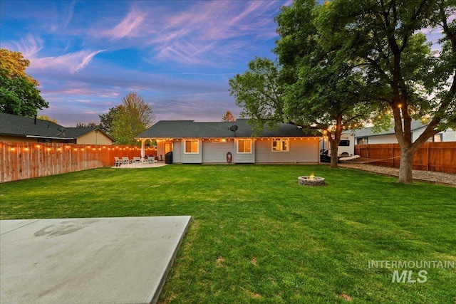 back of house featuring a fenced backyard, a patio, a yard, and a fire pit
