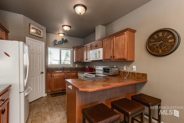 kitchen featuring white appliances, light tile patterned floors, a kitchen breakfast bar, and sink