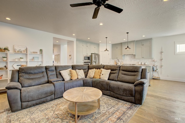 living room with a textured ceiling, light hardwood / wood-style floors, ceiling fan, and sink