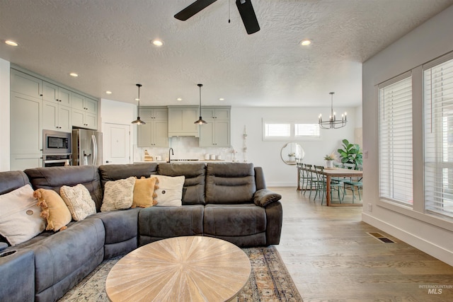 living room with a textured ceiling, light hardwood / wood-style flooring, ceiling fan with notable chandelier, and sink