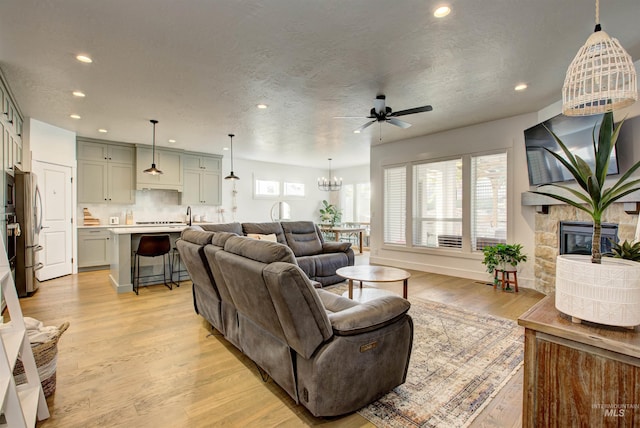 living room featuring a textured ceiling, a fireplace, light hardwood / wood-style flooring, and ceiling fan with notable chandelier