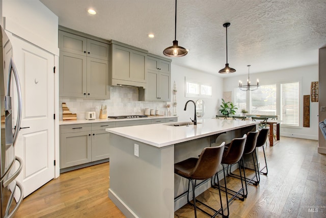 kitchen with sink, stainless steel appliances, an inviting chandelier, an island with sink, and decorative light fixtures