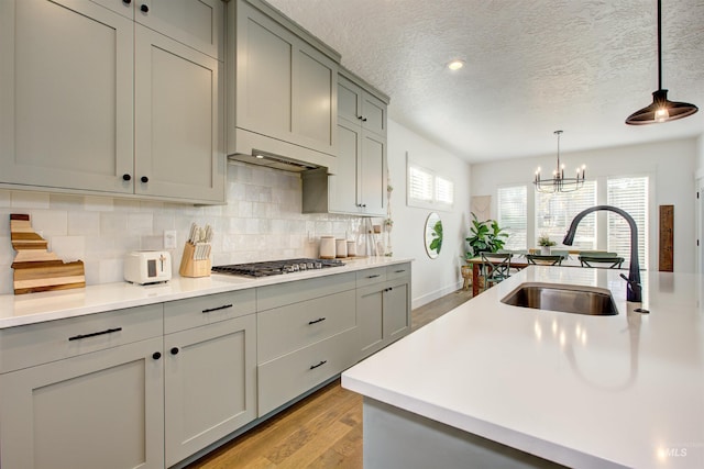 kitchen featuring pendant lighting, stainless steel gas stovetop, sink, a textured ceiling, and a chandelier