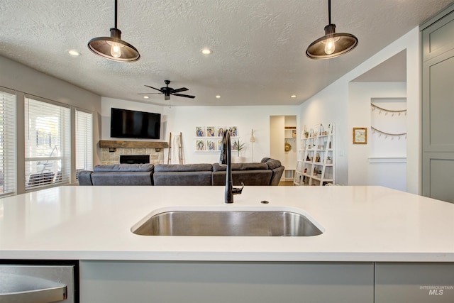 kitchen featuring gray cabinetry, sink, ceiling fan, a fireplace, and a textured ceiling