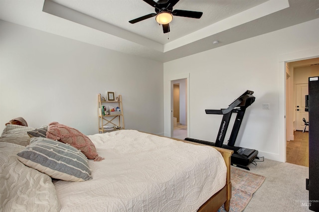 carpeted bedroom with a tray ceiling and ceiling fan