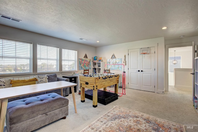 recreation room with a textured ceiling and light carpet