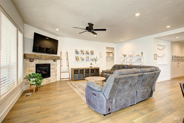 living room featuring ceiling fan, a fireplace, light wood-type flooring, and a textured ceiling