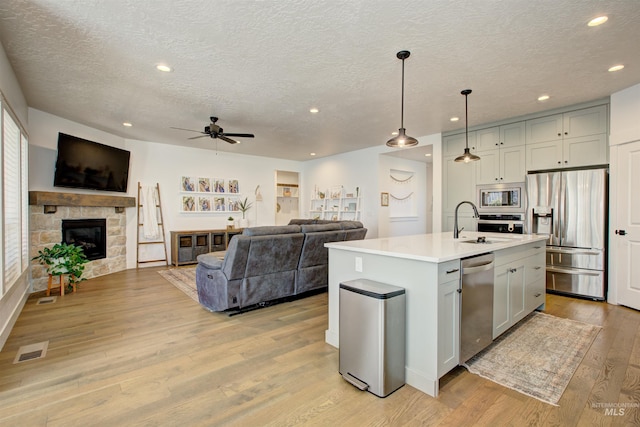 kitchen featuring a kitchen island with sink, hanging light fixtures, ceiling fan, a fireplace, and stainless steel appliances