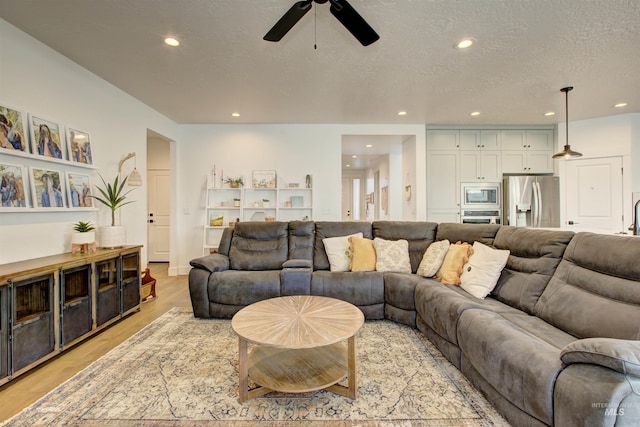 living room featuring ceiling fan, a textured ceiling, and light hardwood / wood-style flooring