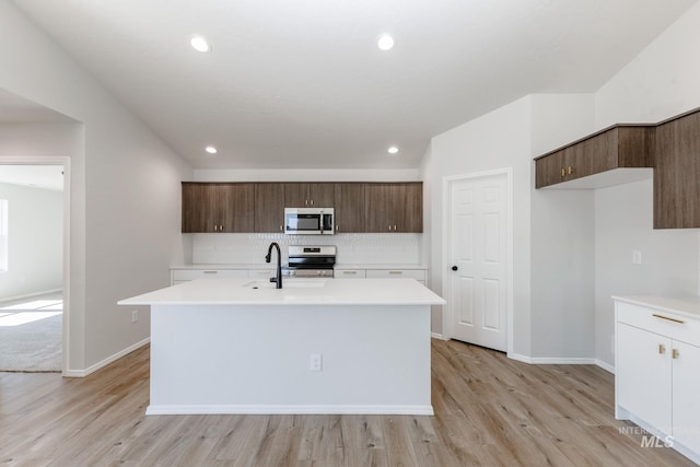 kitchen featuring a center island with sink, light wood-type flooring, light countertops, appliances with stainless steel finishes, and tasteful backsplash