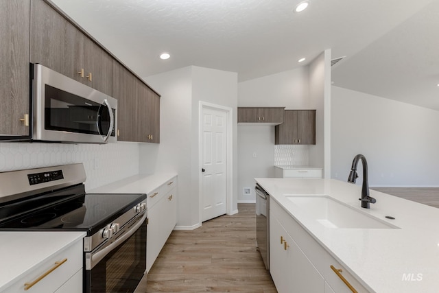 kitchen featuring a sink, light wood finished floors, tasteful backsplash, and appliances with stainless steel finishes