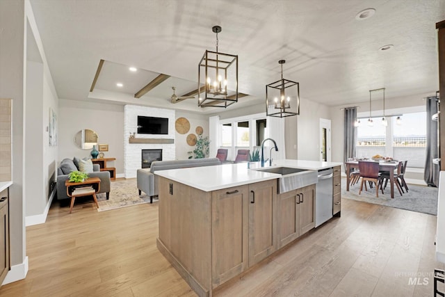 kitchen featuring light wood finished floors, stainless steel dishwasher, a sink, a large fireplace, and light countertops