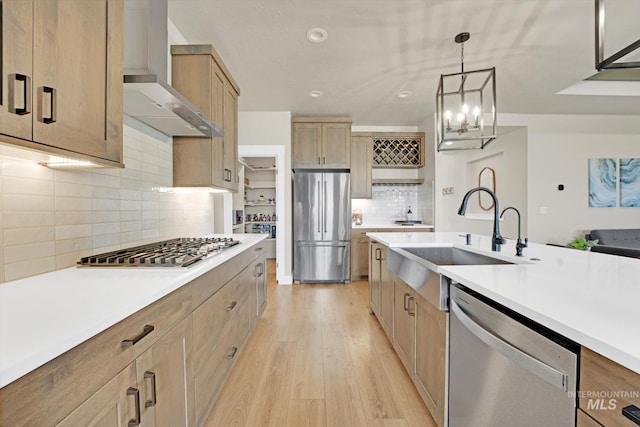 kitchen featuring a sink, stainless steel appliances, light wood finished floors, light countertops, and wall chimney exhaust hood