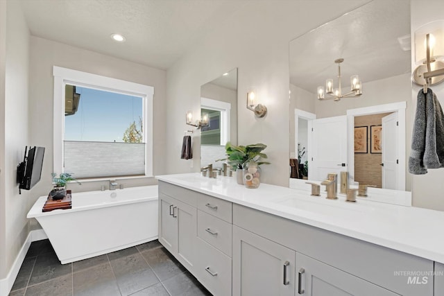 full bathroom with a freestanding bath, double vanity, a sink, and an inviting chandelier