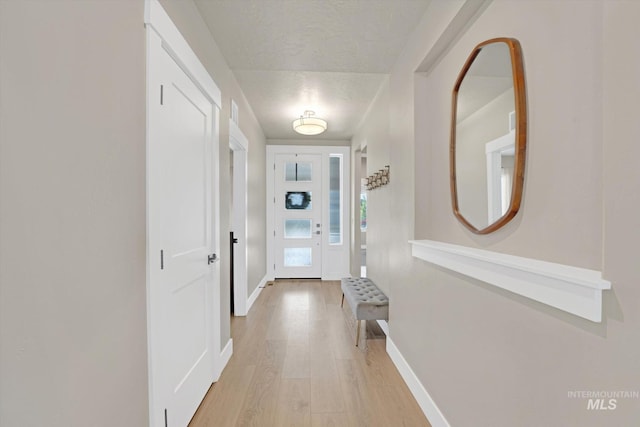 doorway with light wood-type flooring, baseboards, and a textured ceiling