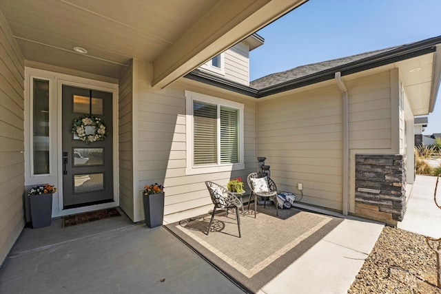 property entrance with a shingled roof and a patio