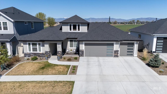 view of front of home featuring a shingled roof, concrete driveway, stone siding, a mountain view, and a garage