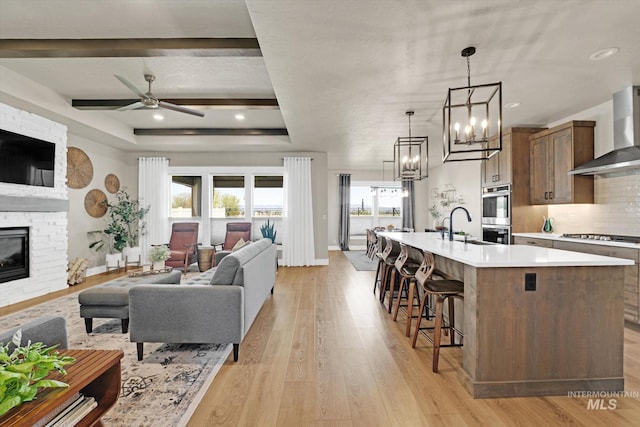 living room featuring light wood finished floors, baseboards, a fireplace, and ceiling fan with notable chandelier