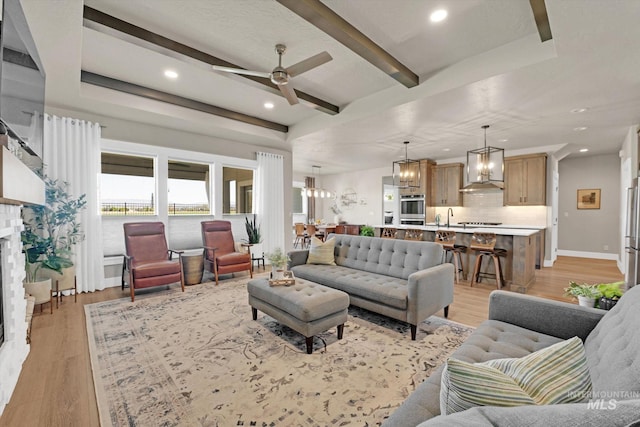 living room with recessed lighting, beamed ceiling, light wood-type flooring, a fireplace, and ceiling fan with notable chandelier