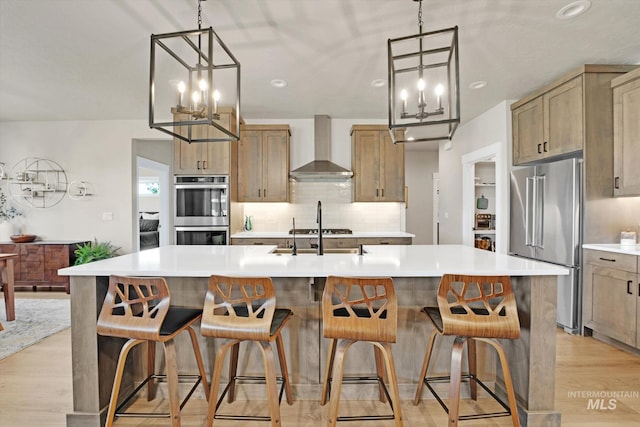 kitchen with a sink, a notable chandelier, appliances with stainless steel finishes, and wall chimney range hood