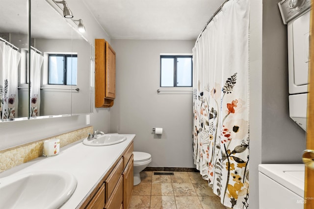 bathroom featuring stacked washer / drying machine, plenty of natural light, toilet, and vanity