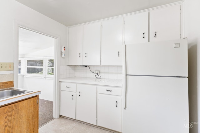 kitchen with light countertops, tasteful backsplash, freestanding refrigerator, and white cabinets