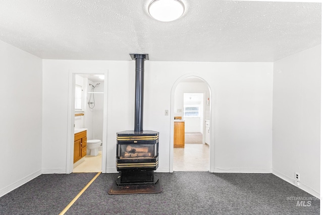unfurnished living room with carpet floors, a wood stove, and a textured ceiling