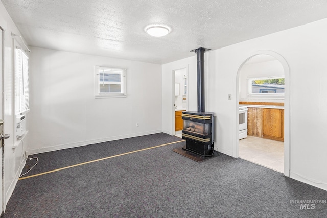 unfurnished living room with carpet flooring, a textured ceiling, a wealth of natural light, and a wood stove