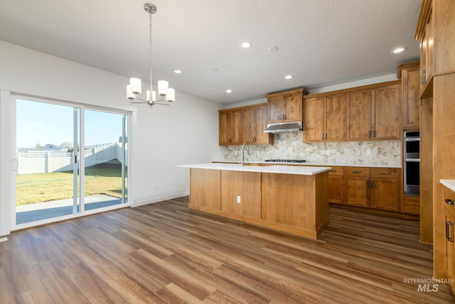 kitchen with hanging light fixtures, dark hardwood / wood-style floors, backsplash, an island with sink, and a chandelier