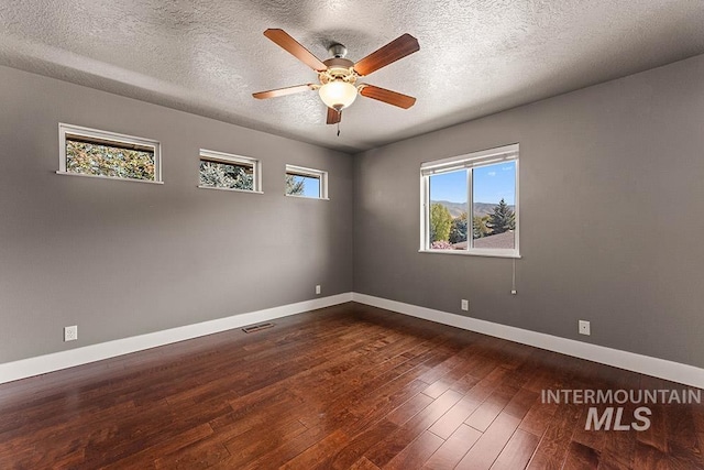 spare room featuring dark wood finished floors, baseboards, ceiling fan, and a textured ceiling