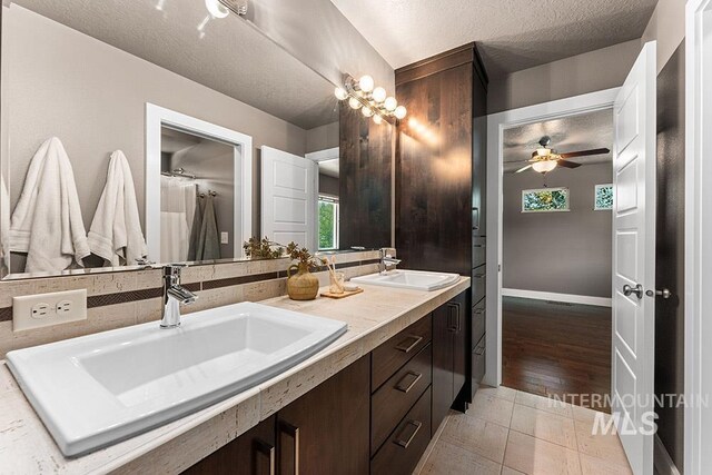 bathroom with ceiling fan, a textured ceiling, double vanity, and tile patterned flooring